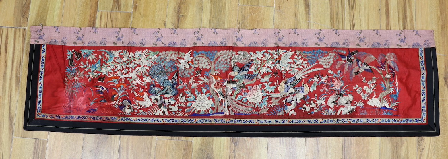 An early 20th century Chinese embroidered silk helmet multi coloured embroidery on a red background depicting oriental birds. 183cm x 47.5cm. 183cm x 47.5cm